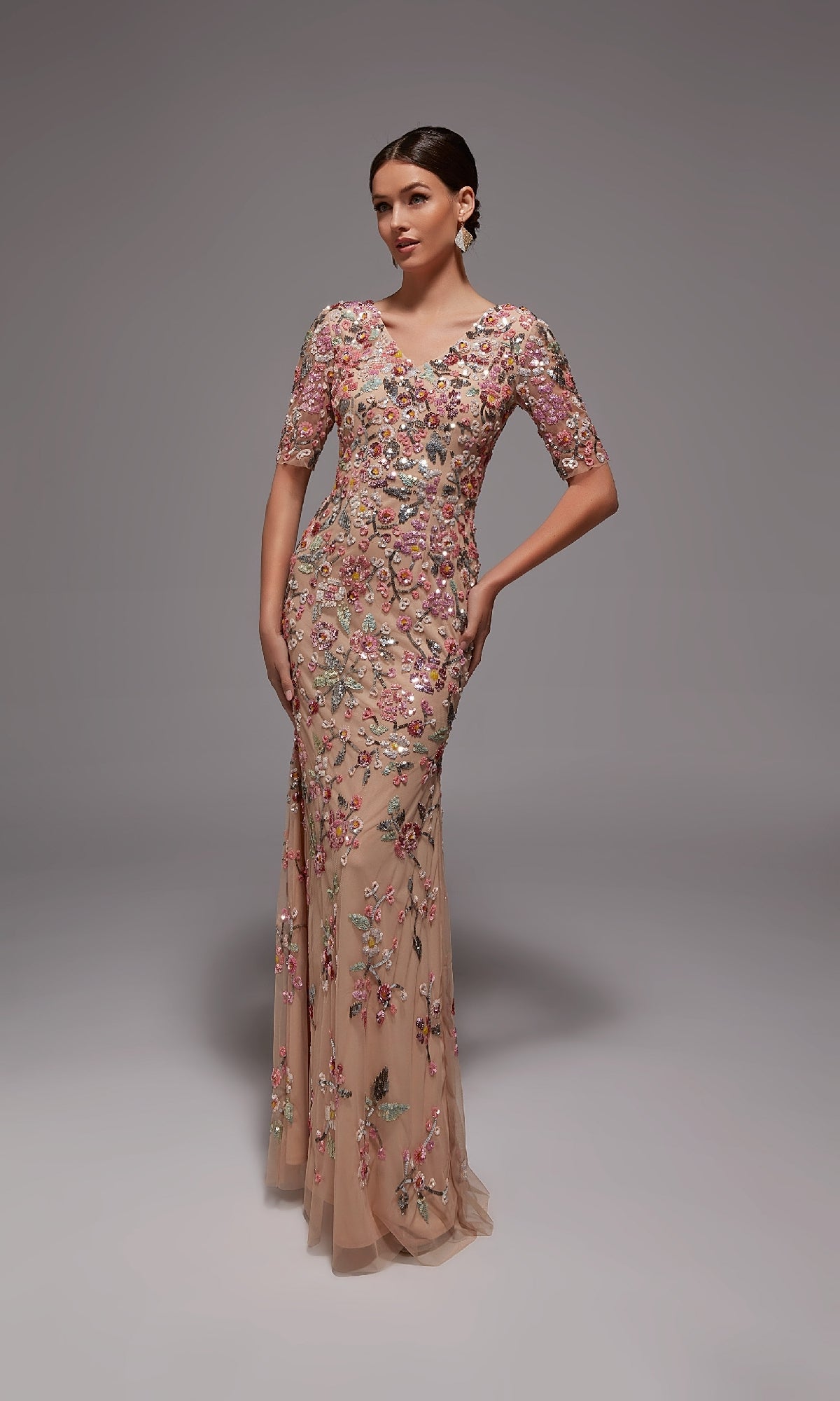 A woman poses gracefully in the Alyce 27848 long formal dress, featuring short sleeves and floral beaded appliques in a floor-length champagne/blush design—ideal for elegant occasions.